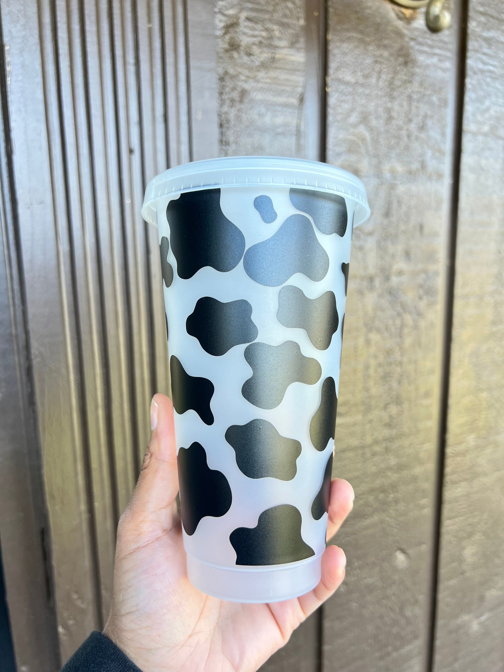 Cow print decorated 24oz cold cup from Daisie Boutique flat lay showing lid straw and full vinyl design detail