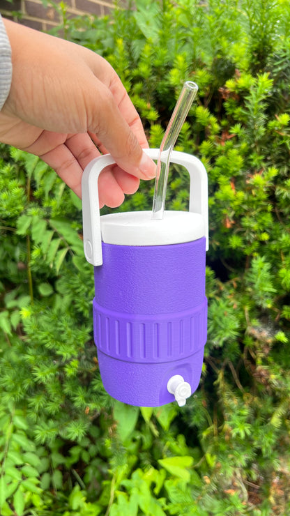Purple and white cooler with a straw and lid held by a hand against a green leafy background